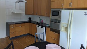 A compact kitchen with wooden cabinets, a microwave, an oven, and a white refrigerator. - A charming countryside accommodation near Malmö (Oxie)