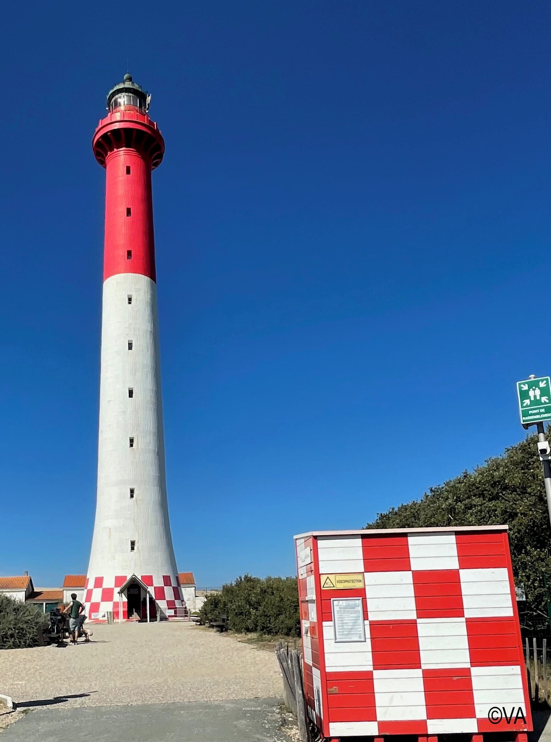 A tall red and white lighthouse with a checkered building nearby.