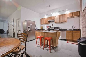A modern kitchen with wooden cabinets, a stainless steel refrigerator, a microwave, and a sink. There is a dining area with a wooden table and chairs.