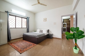 Une chambre à coucher comprenant un lit, une table de chevet, une plante en pot, une fenêtre avec des rideaux et un ventilateur de plafond.