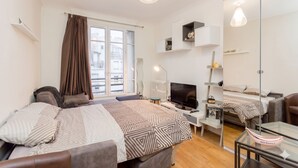 Ett modernt hotellrum med en säng, ett skrivbord med en dator, en tv, en spegel och ett fönster med gardiner.