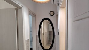 A hallway with a mirror, a clock, and a door leading to a bathroom. - Waterfront Family Apartment (Thessaloniki city)