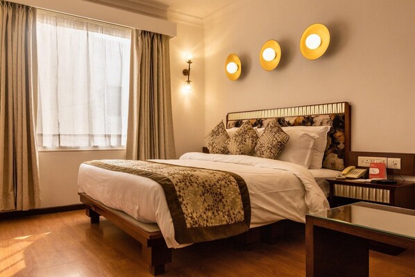 Una habitación de hotel con una cama grande, una mesita de noche con lámpara y una ventana con cortinas.