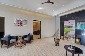 A modern hotel lobby with a seating area, a ceiling fan, and a large window with a view of a golf course.