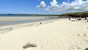 A sandy beach with people, a clear sky, and distant hills.