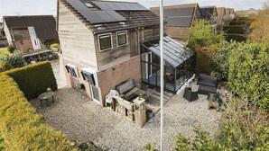 Uma casa moderna com painéis solares, uma estufa de vidro e um pátio de cascalho com mobiliário de exterior.