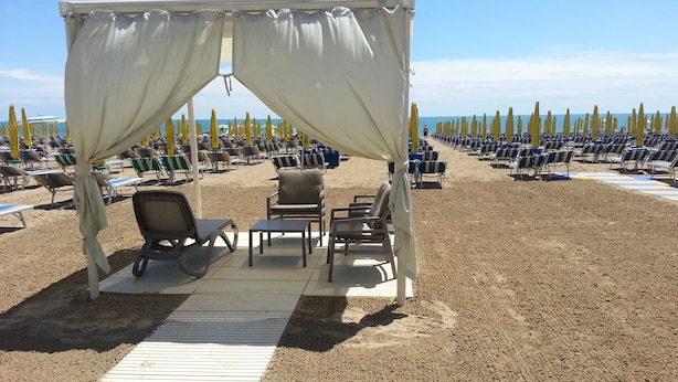 Une plage bordée de rangées de chaises longues et dotée d’un espace de repos abrité, avec une table et des chaises.