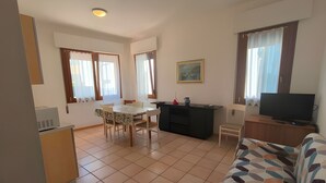 Un salon comprenant un canapé, un téléviseur, une table à manger avec des chaises et un coin cuisine avec un réfrigérateur.