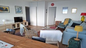 Ein Wohnzimmer mit einem Holzesstisch, einer Couch, einem Fernseher und einem Bücherregal.