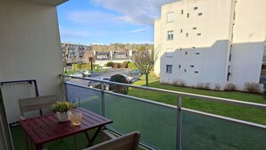 Ein Balkon mit Tisch und Stühlen, einem Blumentopf und Blick auf eine Straße mit parkenden Autos und einem Gebäude im Hintergrund.