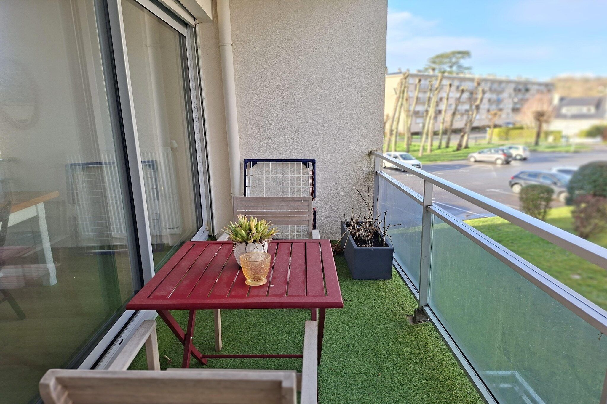 Een balkon met een rode tafel, een bloempot en een metalen rek.