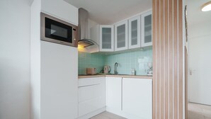 Una cocina compacta con armarios blancos, microondas, tostadora y lavamanos.