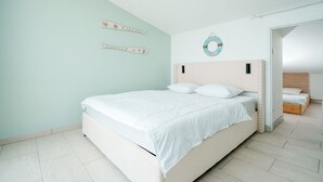 Un dormitorio con cama, cabecera, decoración en la pared y puerta que da a otra habitación.