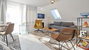 Ein modernes Wohnzimmer mit einer Couch, Sesseln, einem Couchtisch und einem Fernseher.