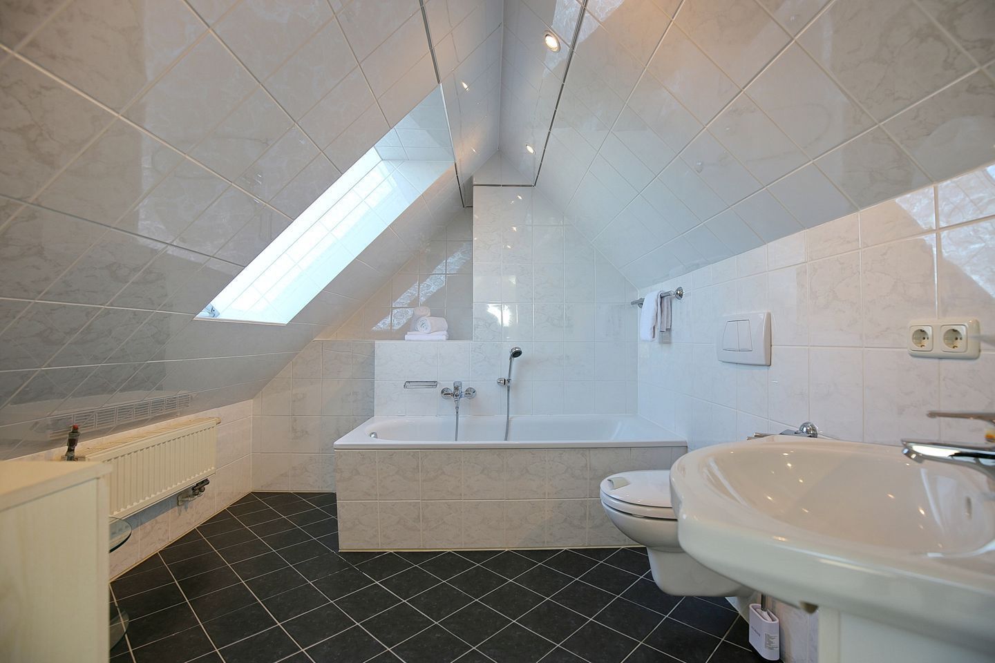 A modern bathroom with a skylight, a bathtub, a toilet, and a sink.