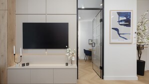 Ein moderner Empfangsbereich mit Flachbildfernseher, einer Konsole mit Dekoration, einem gerahmten abstrakten Kunstwerk und einer Topfpflanze.