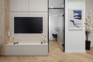 A modern reception area with a flat-screen TV, a console table with decorative items, a framed abstract artwork, and a potted plant. - Modern Apartment in the Center | Air Conditioning | Place to Work (Warszawa)