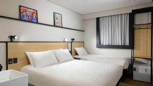 Une chambre d’hôtel avec deux lits, un bureau, une petite armoire et une fenêtre avec des rideaux.