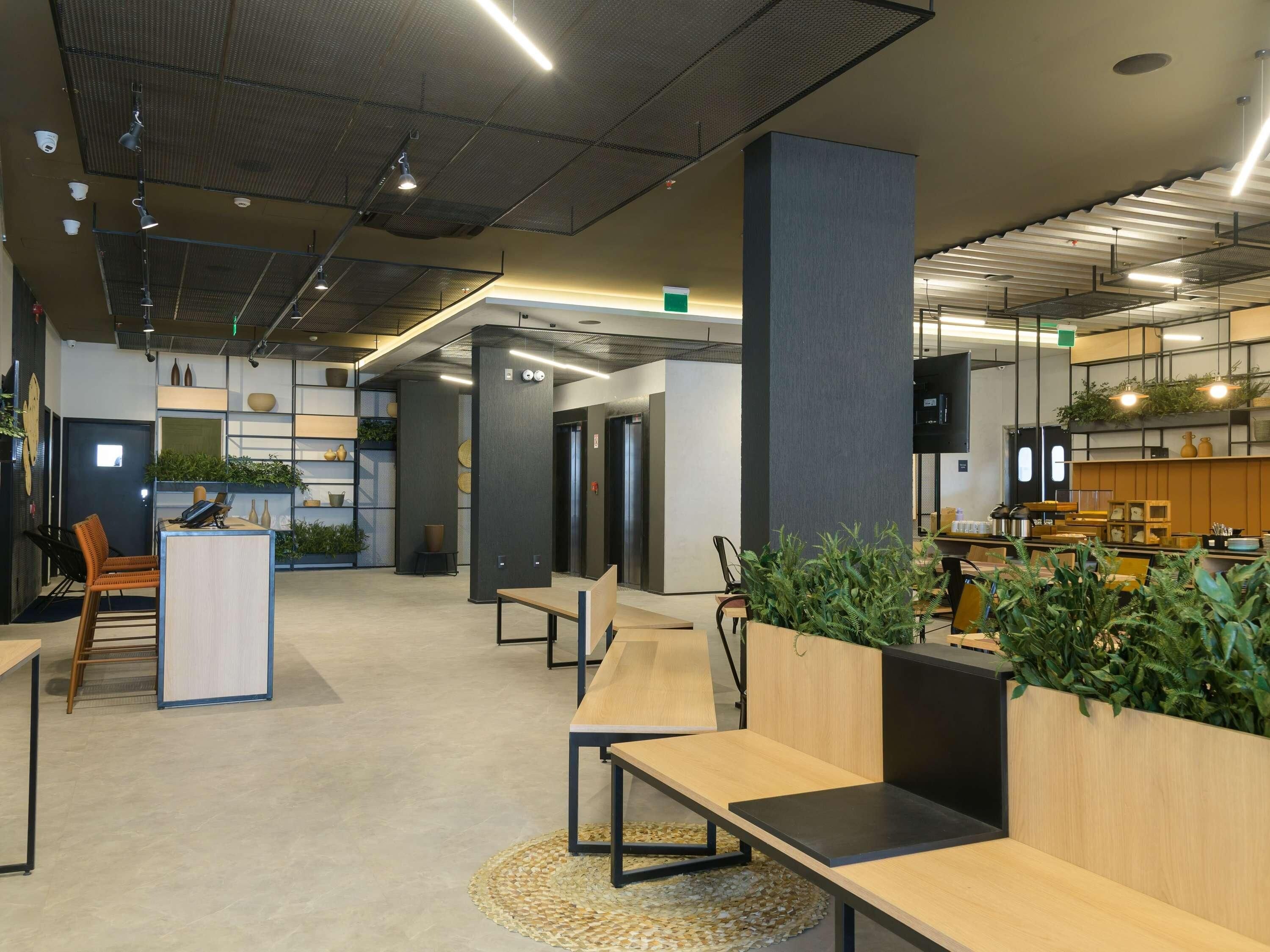 Um espaço de escritório moderno com mesas em plano aberto, cadeiras ergonômicas e iluminação natural e artificial.