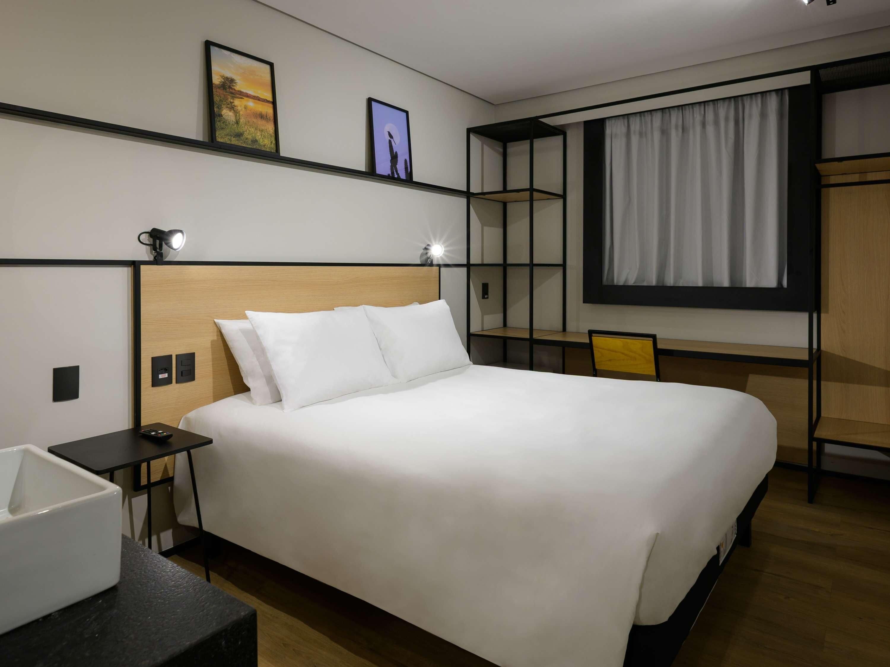 Quarto de hotel moderno com uma cama grande, mesas de cabeceira, escrivaninha e um guarda-roupa.