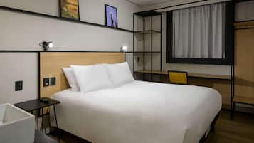 Quarto de hotel moderno com uma cama grande, mesas de cabeceira, escrivaninha e um guarda-roupa.