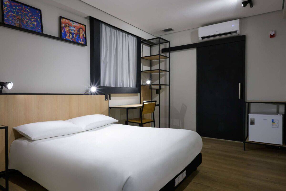 Una habitación de hotel con cama, escritorio, silla, armario y unidad de aire acondicionado.