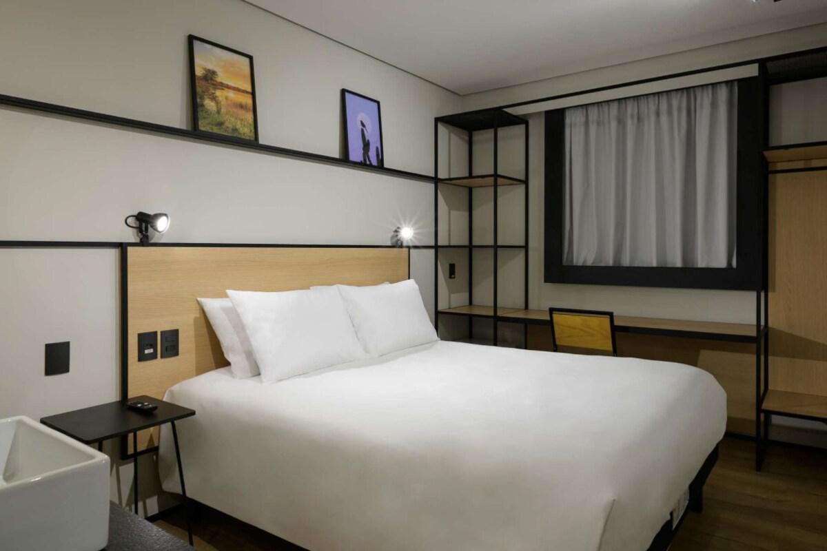 Ein Hotelzimmer mit einem großen Bett, Nachttischen, einem Schreibtisch, einem Stuhl und einem fensterbepflanzten Fenster.