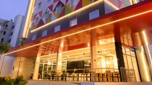 Un hôtel à plusieurs étages, doté d’une façade aux motifs géométriques et aux couleurs vives, de grandes fenêtres et d’un espace extérieur aménagé avec des sièges.
