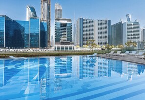 Una piscina moderna in hotel con acqua cristallina, circondata da grattacieli e un'area verde curata.