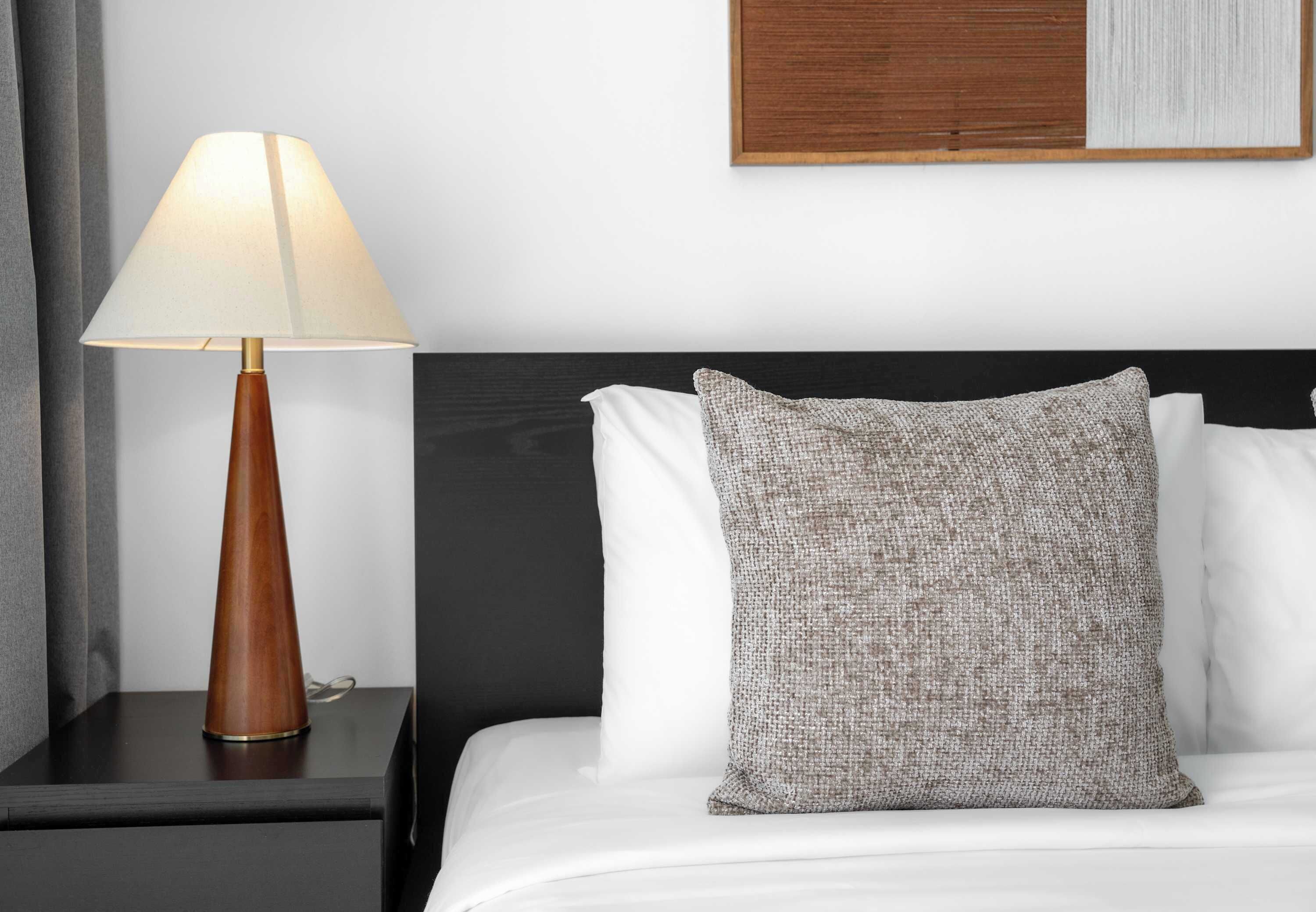Una cama bien hecha con un almohadón texturizado y una mesita de noche de madera con lámpara.
