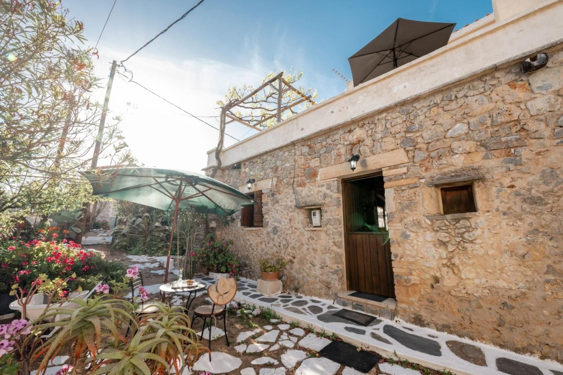 A stone building with a wooden door, a small window, and a stone-paved patio with a table and chairs.