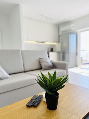 Un salon moderne avec un canapé blanc, une petite plante en pot posée sur une table basse en bois et deux télécommandes.