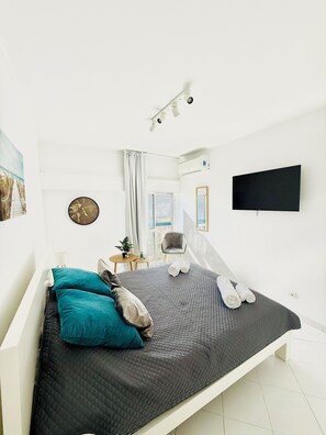 Une chambre à coucher moderne avec un lit, une horloge, un téléviseur et une fenêtre avec des rideaux.