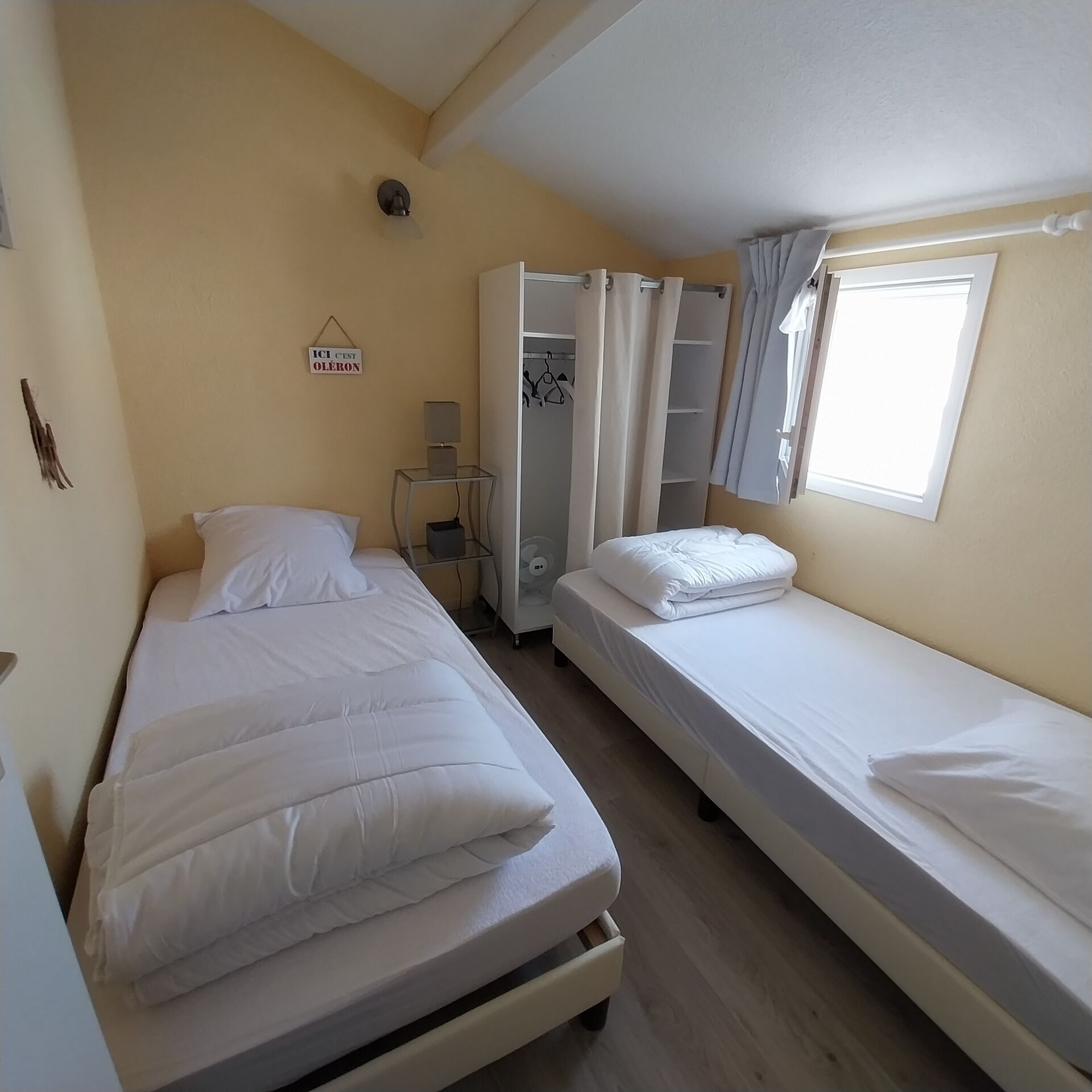 A room with two beds, a wardrobe, a small table with a lamp, and a sign on the wall.