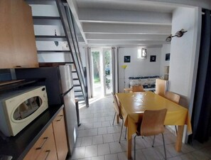Una cocina compacta con microondas, una mesa de comedor con sillas y una escalera que lleva a un espacio exterior.