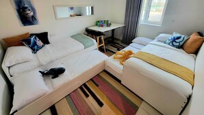 Hotellihuone, jossa on kaksi sänkyä, työpöytä, peili ja ikkuna, jossa on verhot.