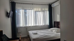 Une chambre d’hôtel équipée d’un lit, d’un bureau, d’une chaise, d’une fenêtre avec des rideaux et d’un appareil de climatisation.