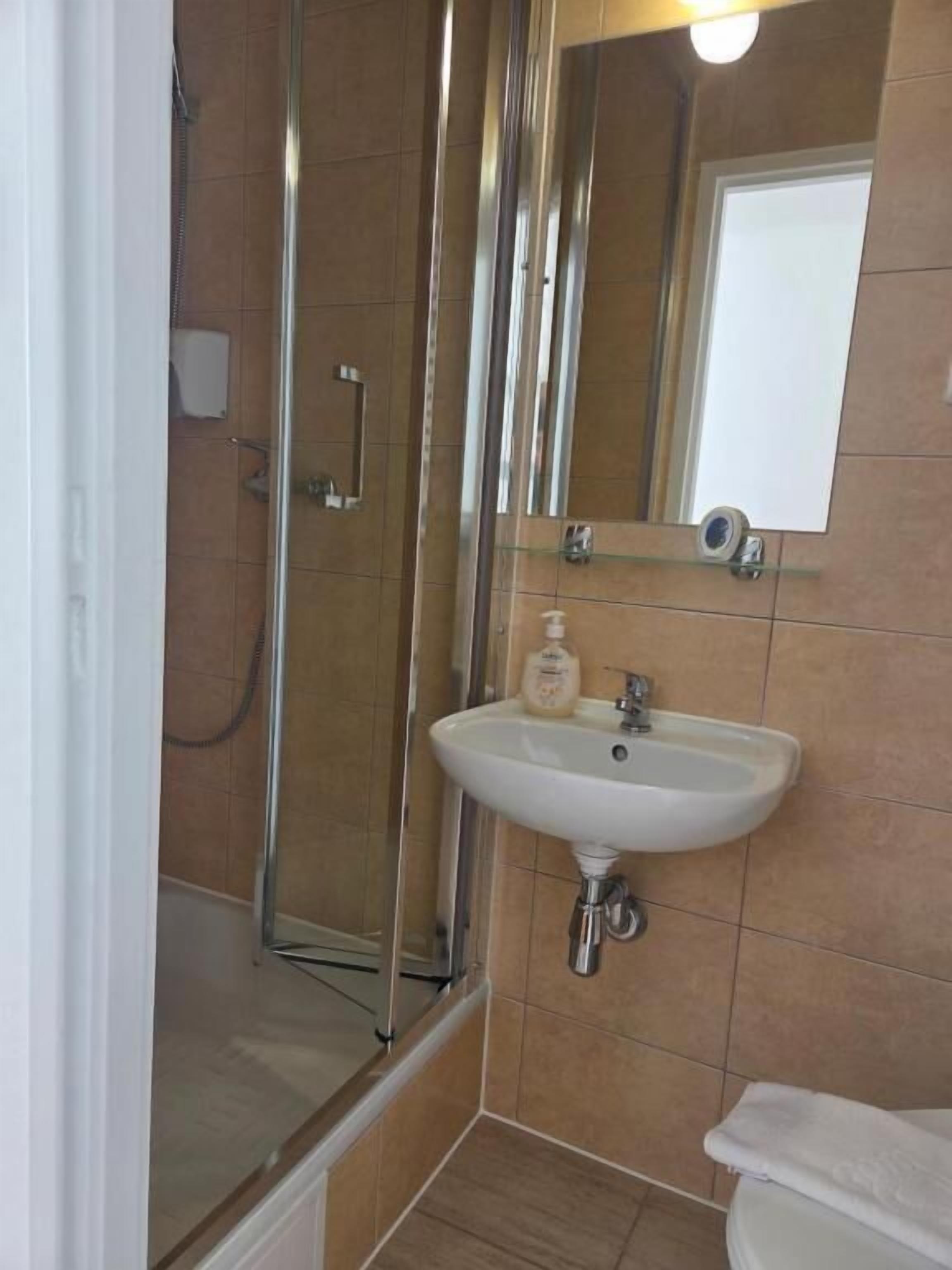 A bathroom with a glass shower enclosure, a sink with a mirror above it, and a toilet.