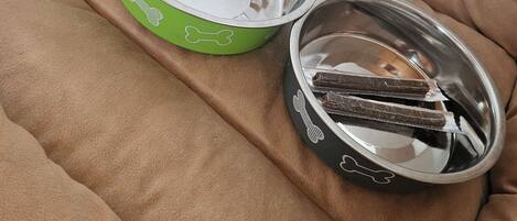 A pet bed with two metal bowls, one green and one black, containing food.