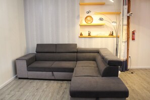 Un salon moderne avec un canapé d’angle, un plancher en bois et une étagère murale agrémentée d’objets décoratifs.