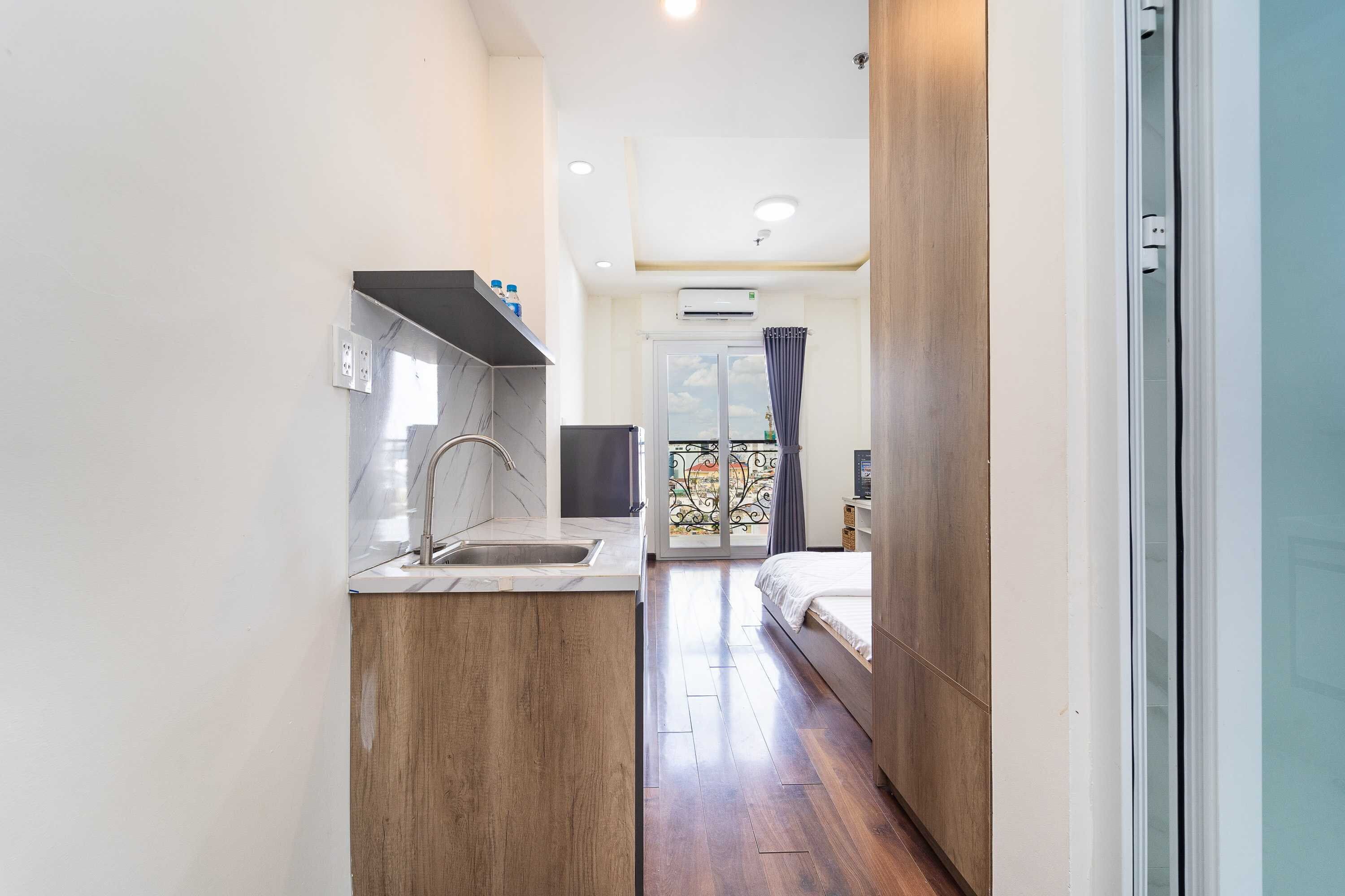A narrow hallway leading to a bedroom with a large window, a kitchen area with a sink and a stove, and a radiator.