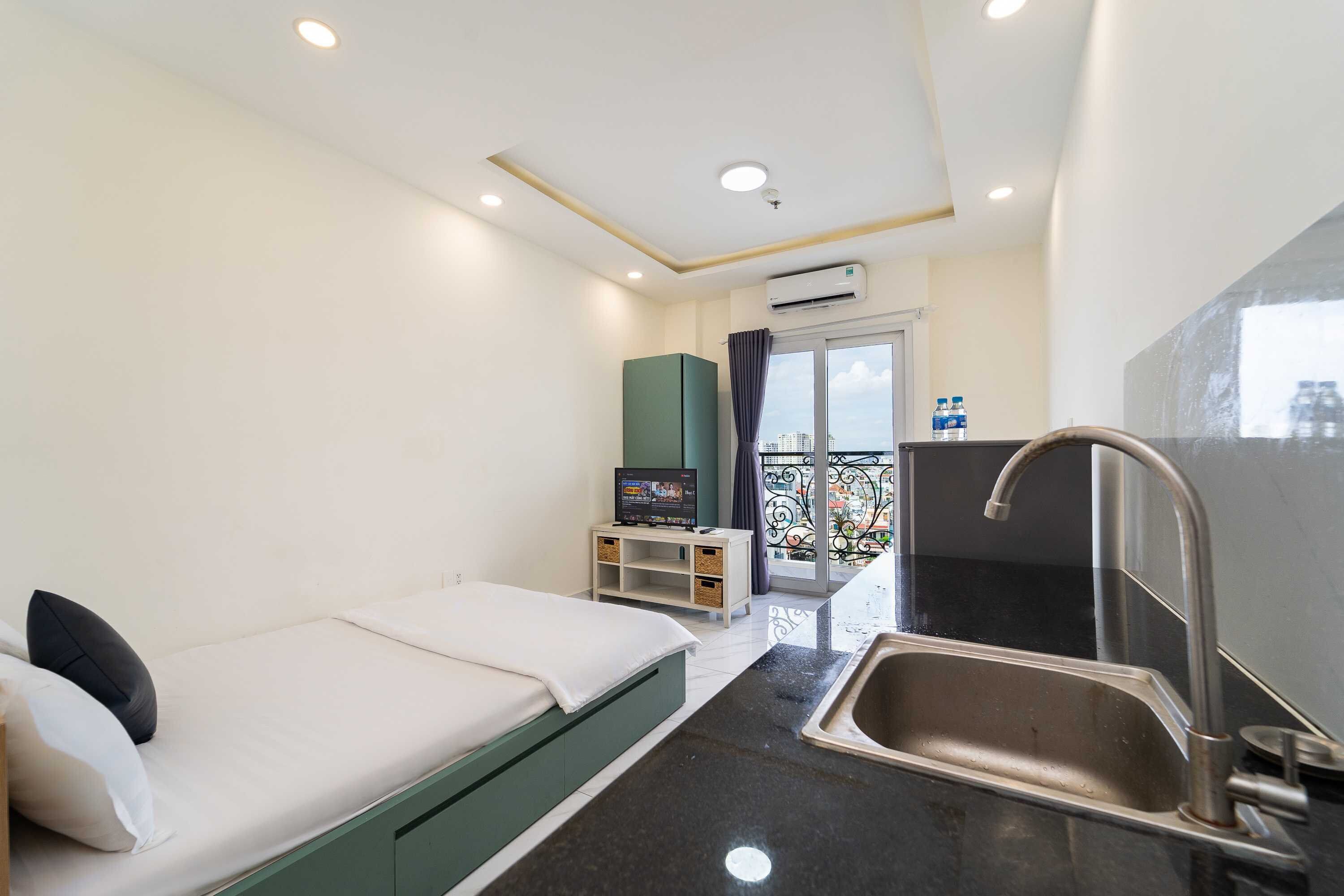 A compact hotel room with a bed, a small kitchenette, a window with a view, and a balcony.