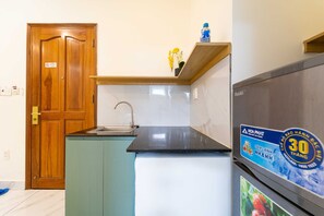 A compact kitchen with a wooden door, a small countertop, a sink, and a refrigerator with a water bottle on top. - Palette Phu Nhuan Apartment (Ho Chi Minh City)