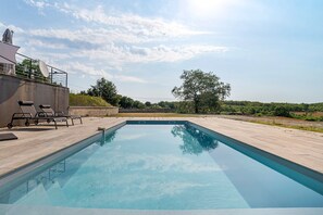 Une piscine rectangulaire à l’eau d’un bleu limpide, entourée d’une terrasse en béton.