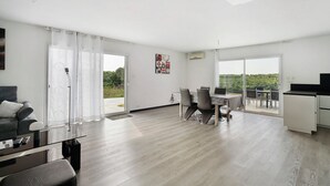 Een moderne woonkamer met een glazen salontafel, een bank, een eethoek met tafel en stoelen, en een keuken met een televisie.