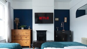 Un dormitori amb un televisor que mostra "NETFLIX", un taulell de nit de fusta, un armari fosc i una llar de foc.