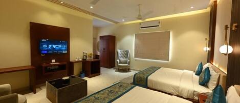 A hotel room with two beds, a television, a ceiling fan, and a window with blinds.