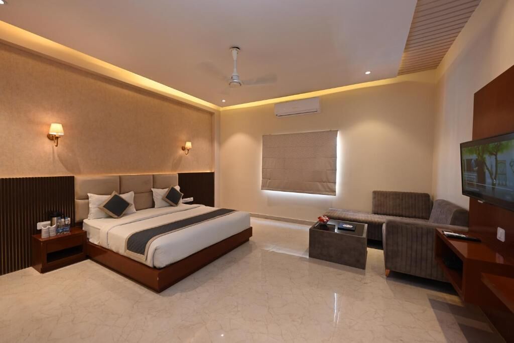 A modern hotel room with a large bed, a sofa, a coffee table, and a flat-screen TV.