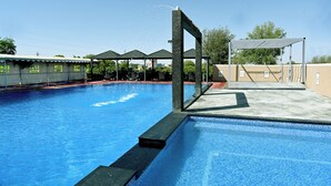 A swimming pool with a diving platform, surrounded by covered areas and a clear sky. - THE GANGA RESORT (Bikaner)