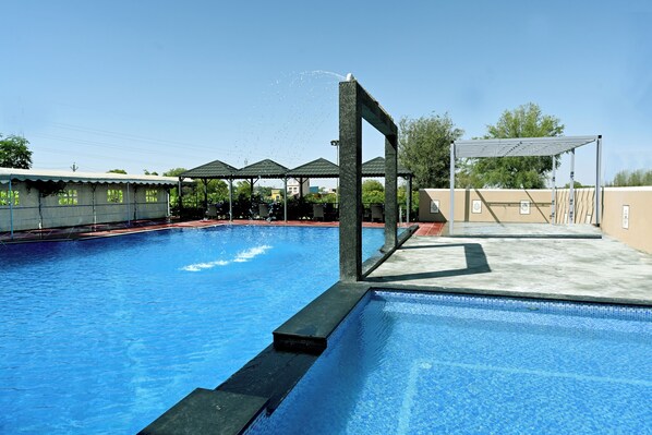 A swimming pool with a diving platform, surrounded by covered areas and a clear sky. - THE GANGA RESORT (Bikaner)